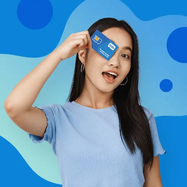 Young woman with dark hair holding a Tello SIM card up to her eye against a blue wave-patterned background