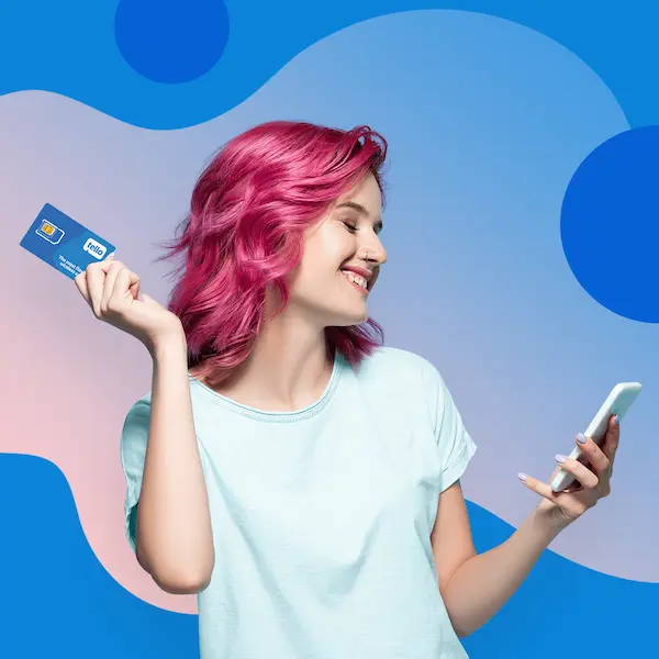 Woman with pink hair holding a Tello SIM card while looking at her phone