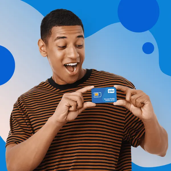 Young man in a striped shirt smiling while holding a Tello SIM card with both hands